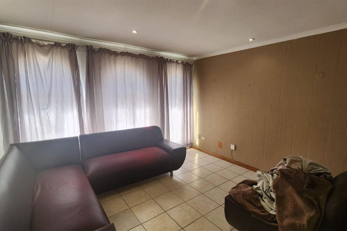 A living room featuring ceramic tiled flooring and recessed downlighting, currently requiring cosmetic updates to the wall finishes.