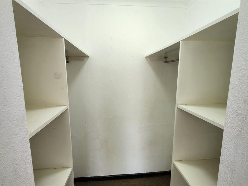 A walk-in closet space featuring built-in shelving and hanging rails, currently empty and showing signs of wear on the wall surfaces.
