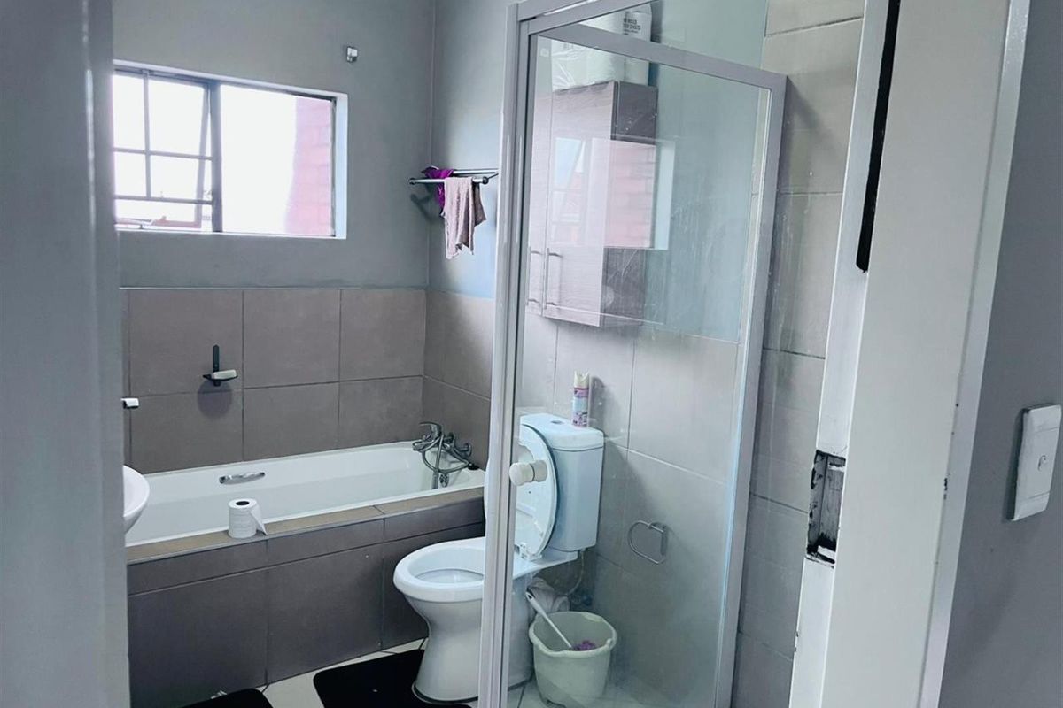 A functional bathroom featuring a built-in bathtub, a separate glass-enclosed shower, a toilet, and neutral wall tiling.