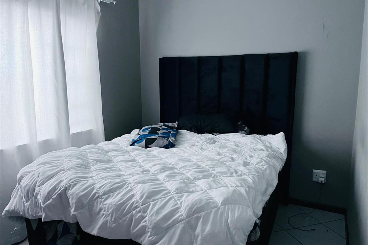 A bedroom featuring tiled flooring and neutral grey walls, providing a functional space for rest.