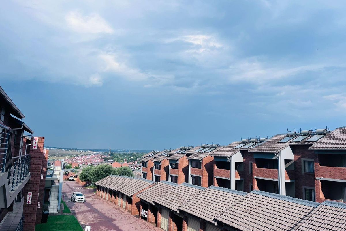 Elevated view of the apartment complex, featuring brick facade buildings, tiled roofing, solar geysers, and a paved driveway with garage units.