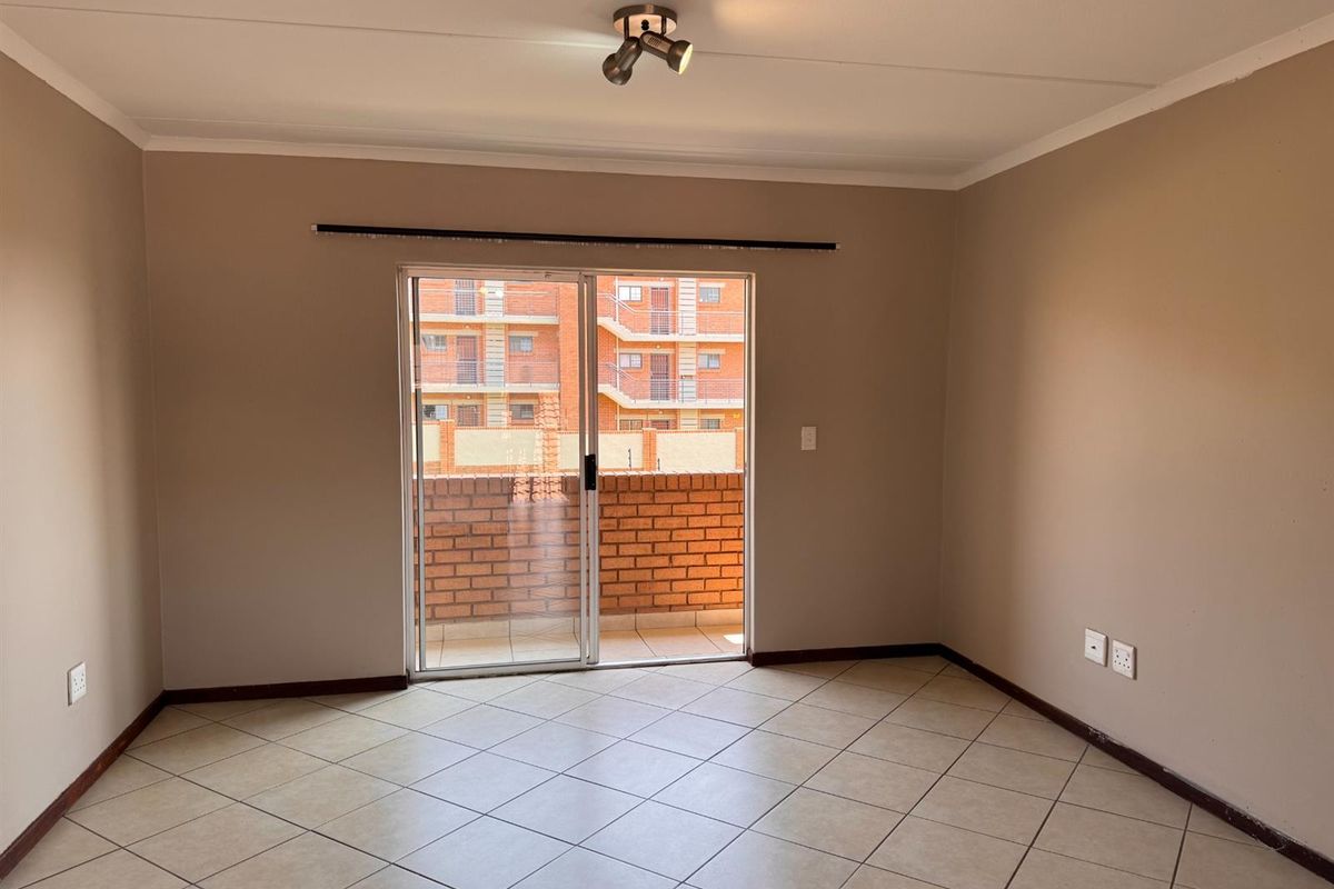 An empty, well-lit living room featuring neutral tiled flooring and a sliding glass door providing access to a private balcony.