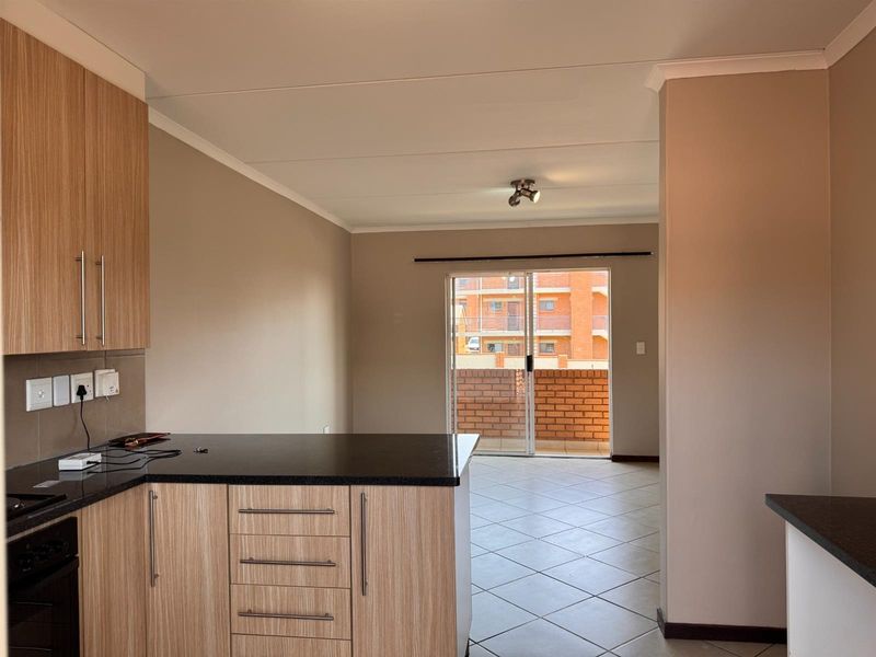 An open-plan kitchen and living area featuring modern wood-finish cabinetry, granite countertops, tiled flooring, and a sliding door leading to a balcony.