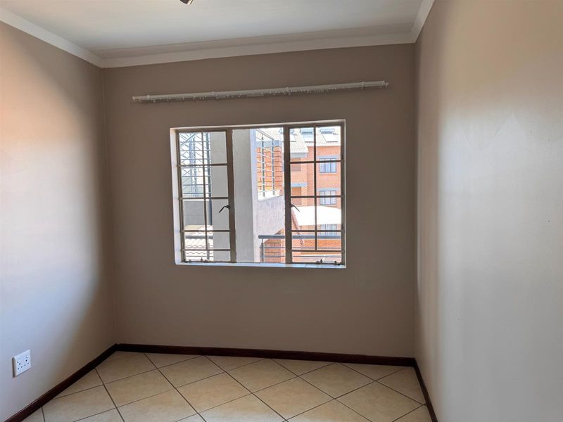 An empty bedroom featuring neutral wall paint, tiled flooring, and a window fitted with security bars and a curtain rail.
