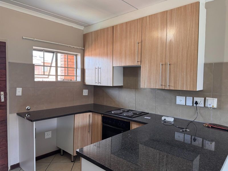 A functional kitchen featuring light wood-finish cabinetry, dark granite countertops, a built-in electric hob and oven, and neutral tiled backsplash.