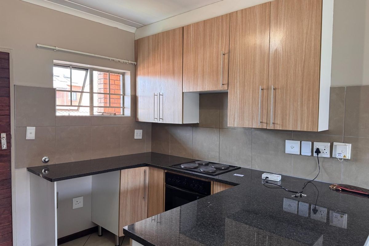 A functional kitchen featuring light wood-finish cabinetry, dark granite countertops, a built-in electric hob and oven, and neutral tiled backsplash.