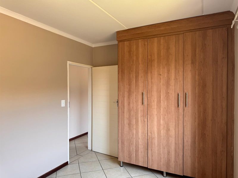 A clean, empty bedroom featuring neutral wall tones, tiled flooring, and ample built-in wooden cupboards for storage.