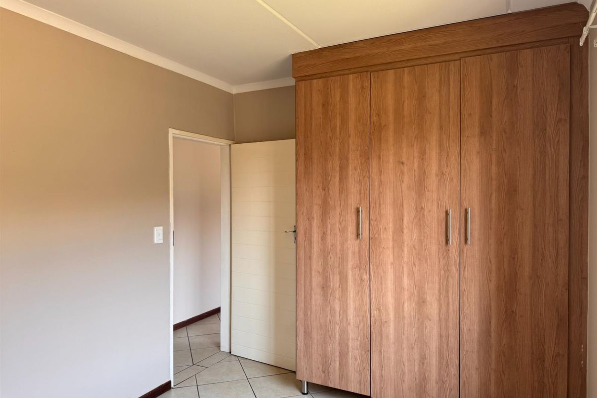 A clean, empty bedroom featuring neutral wall tones, tiled flooring, and ample built-in wooden cupboards for storage.