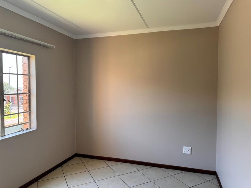 A clean, empty bedroom featuring neutral wall paint, tiled flooring, and a steel-framed window, providing a versatile space ready for personalization.