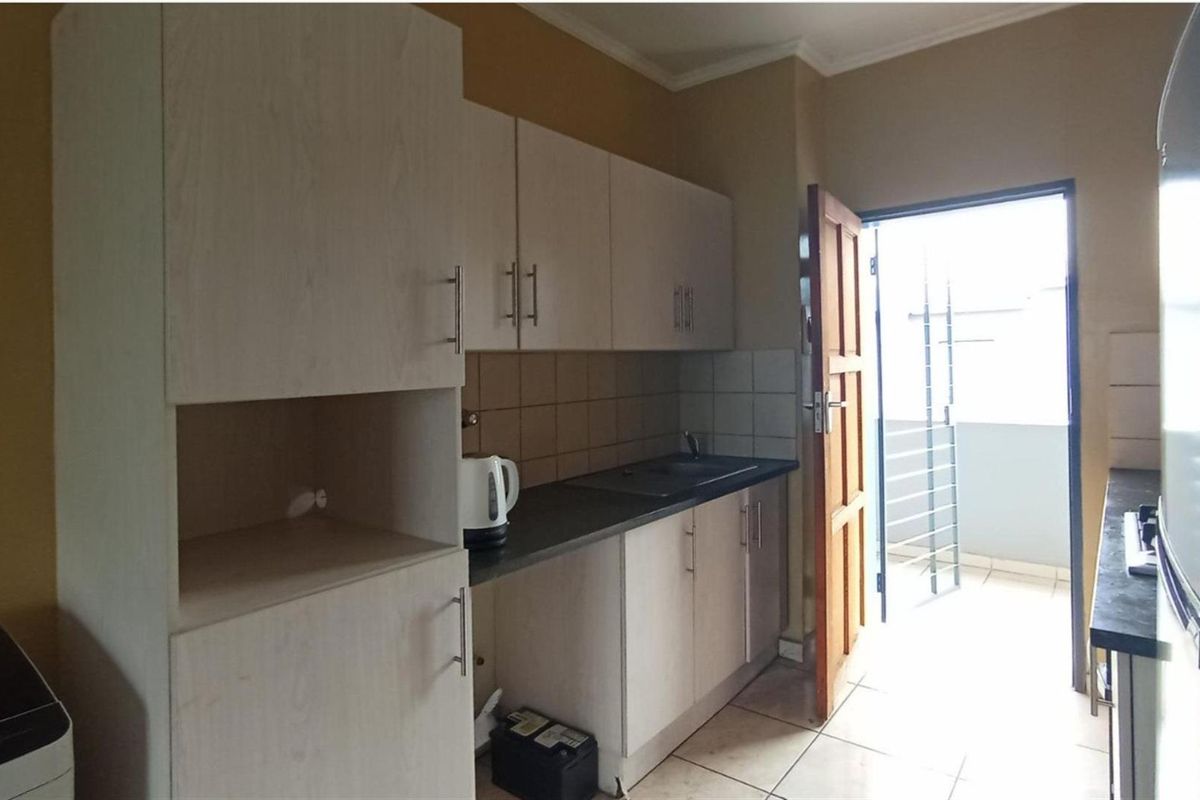 A functional kitchen featuring light-toned cabinetry, dark countertops, tiled splashbacks, and direct access to an outdoor balcony area.