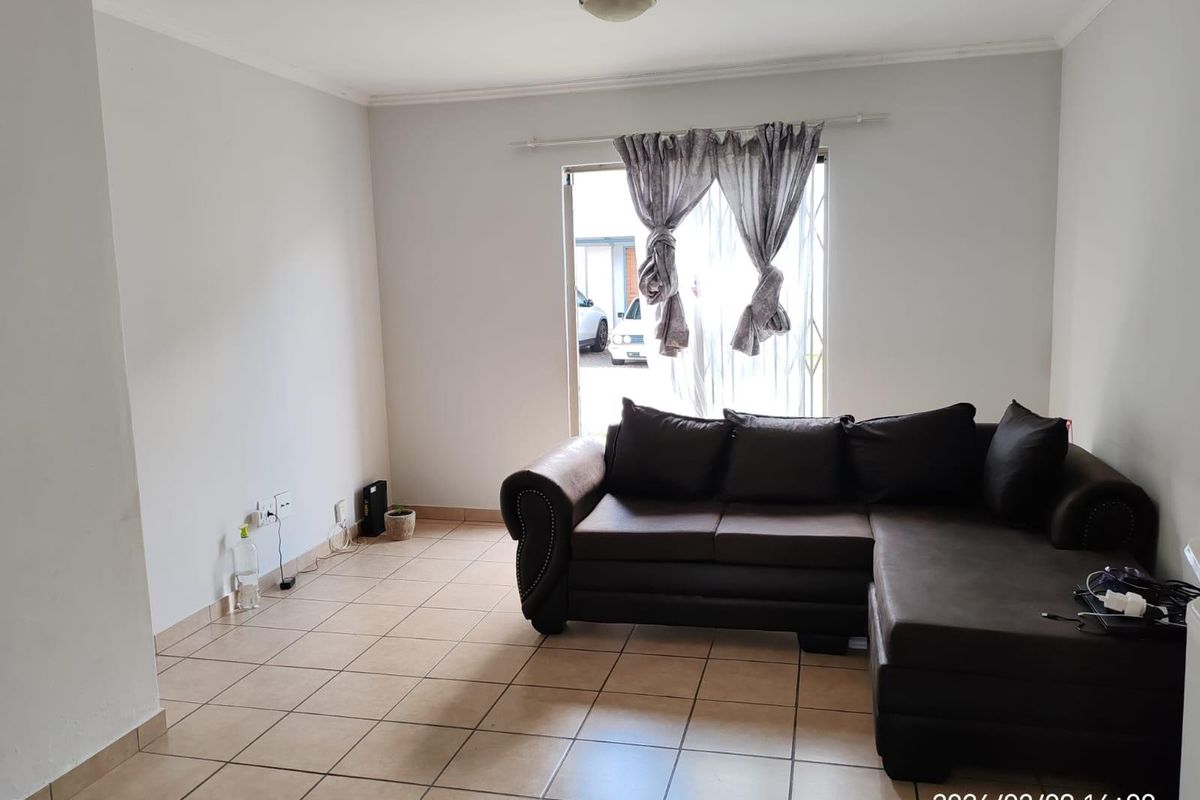 A living room featuring tiled flooring and a sliding glass door with security gate, providing access to the exterior.