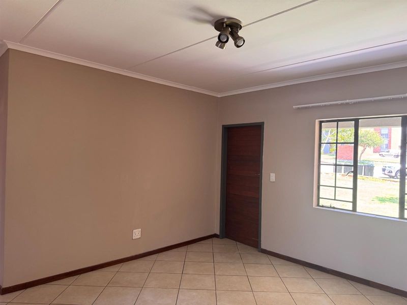 An empty living room featuring neutral wall paint, tiled flooring, a ceiling spotlight fixture, and a window with security bars.