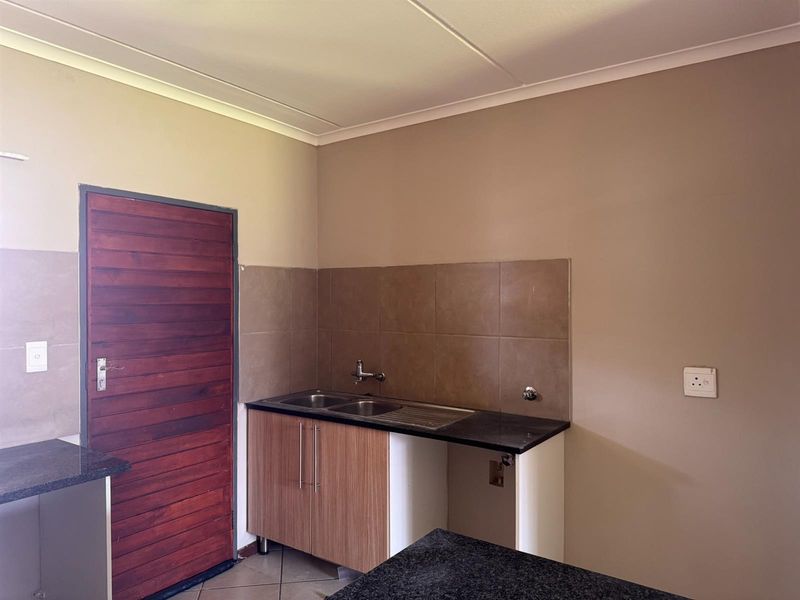 A functional kitchen area featuring granite countertops, a double bowl stainless steel sink, tiled splashback, and built-in cabinetry.
