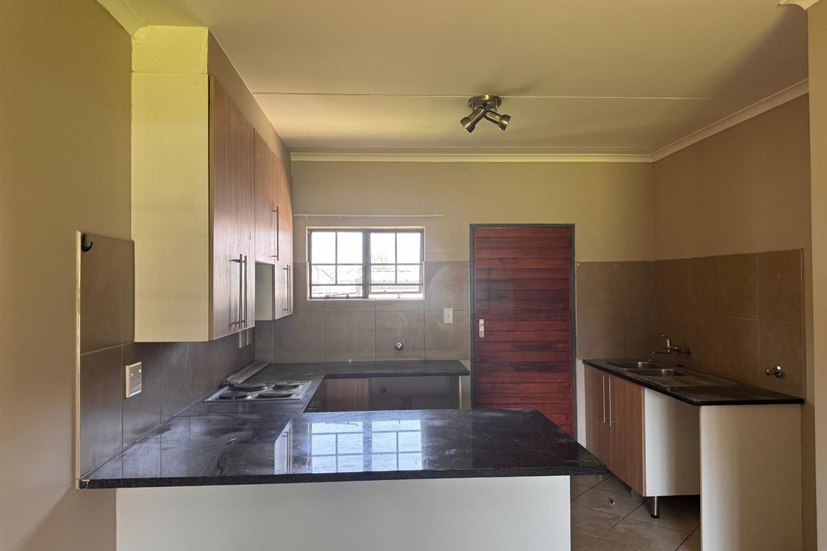 A functional kitchen featuring granite countertops, built-in cabinetry, an electric hob, and a double sink with tiled backsplash and flooring.