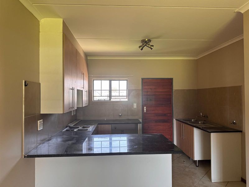 A functional kitchen featuring granite countertops, built-in cabinetry, an electric hob, and a double sink with tiled backsplash and flooring.