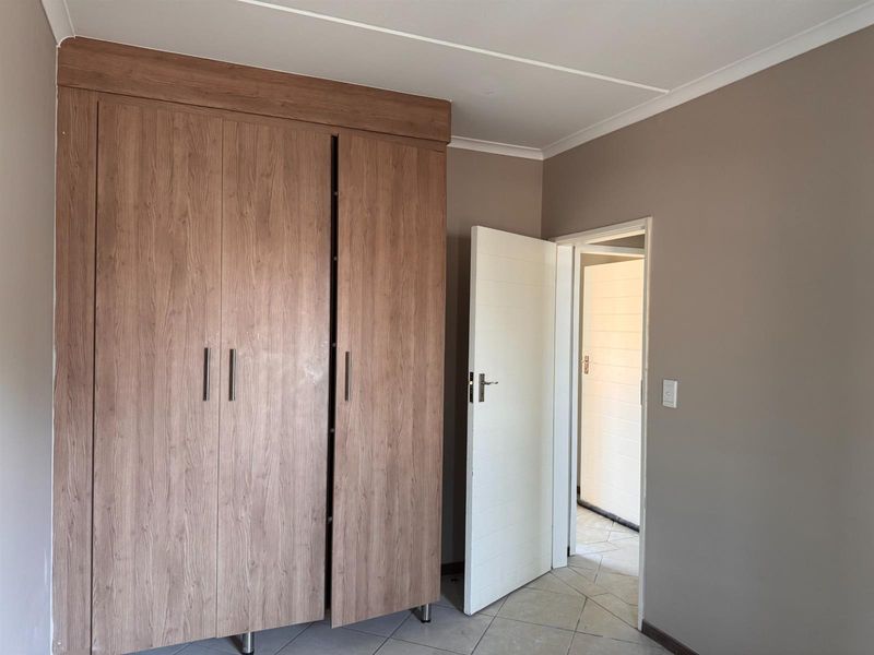 A clean, empty bedroom featuring neutral wall tones, tiled flooring, and a large built-in wooden wardrobe.