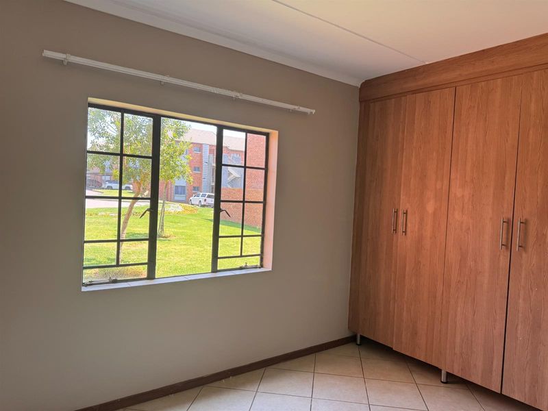 A bright, empty bedroom featuring tiled flooring and a large built-in wooden wardrobe with ample storage space.