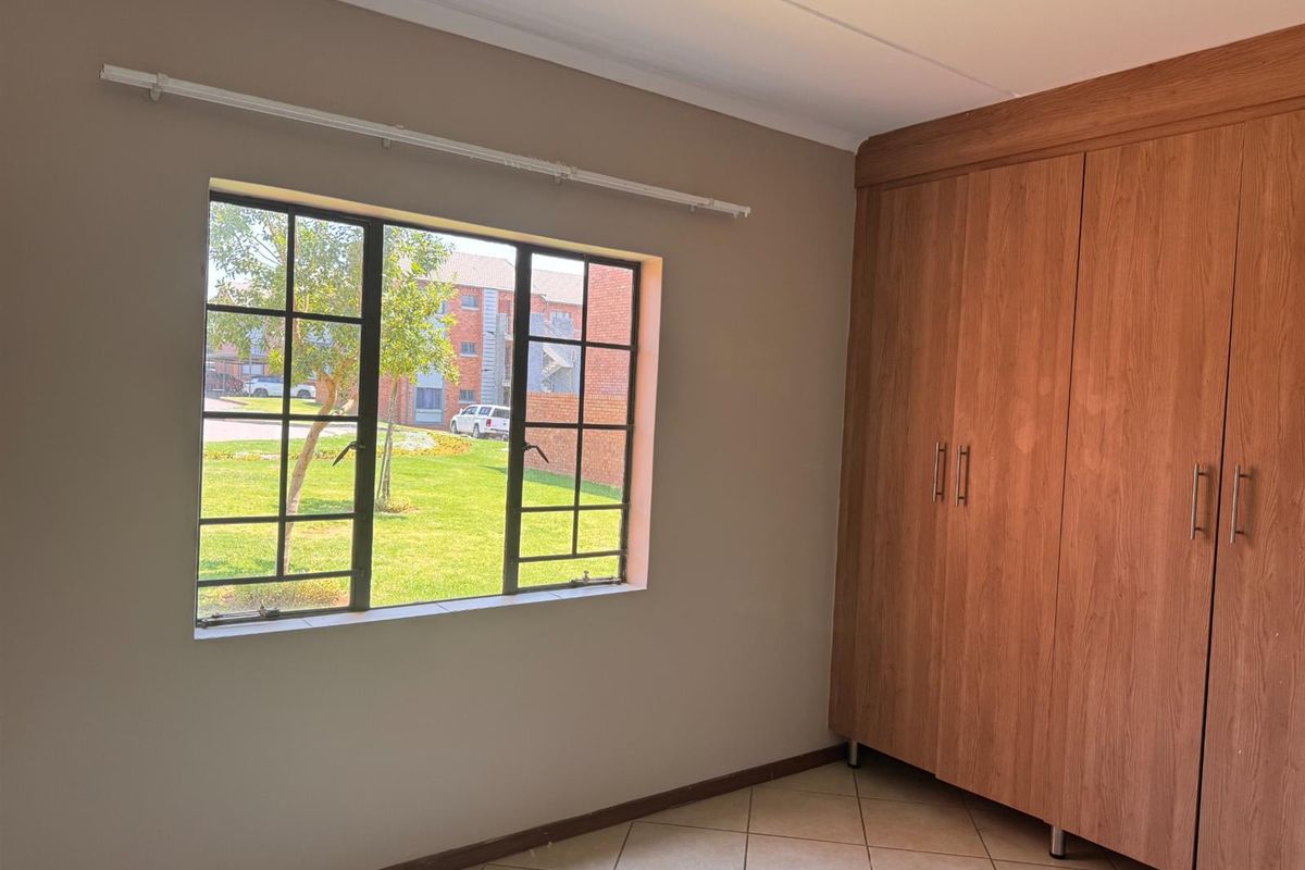 A bright, empty bedroom featuring tiled flooring and a large built-in wooden wardrobe with ample storage space.