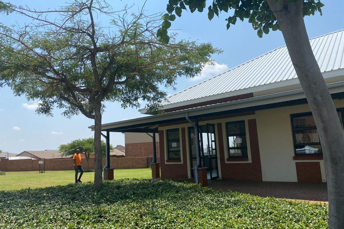 A well-maintained exterior view of the property featuring a brick facade, corrugated metal roof, and a paved patio area overlooking a landscaped garden.