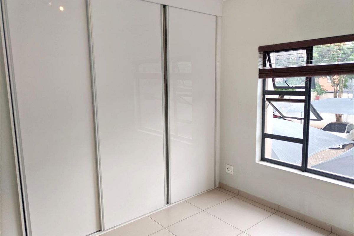 A bright bedroom featuring modern white built-in sliding door cupboards and tiled flooring, complemented by a window with fitted blinds.