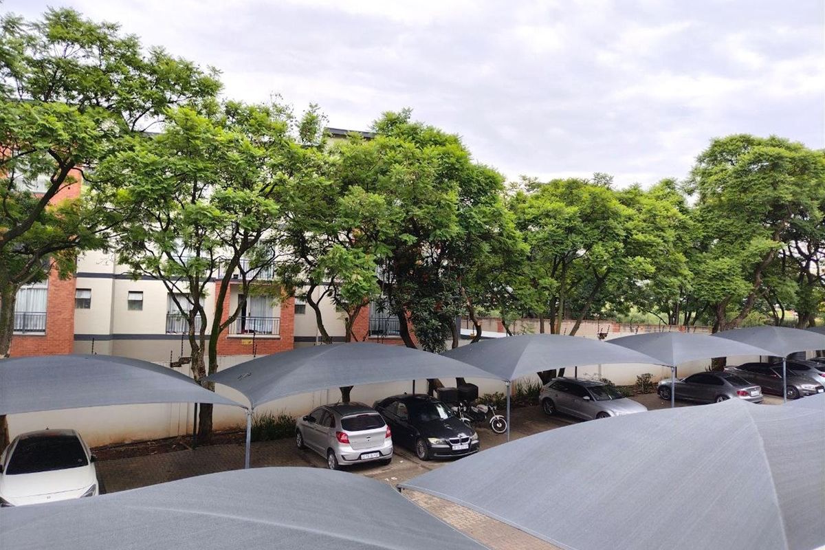 An elevated view of the apartment complex parking area featuring multiple shade-cloth carports and mature trees.