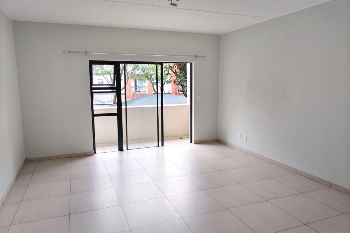 A bright, empty living room featuring neutral floor tiles and large sliding glass doors that open onto a private balcony.