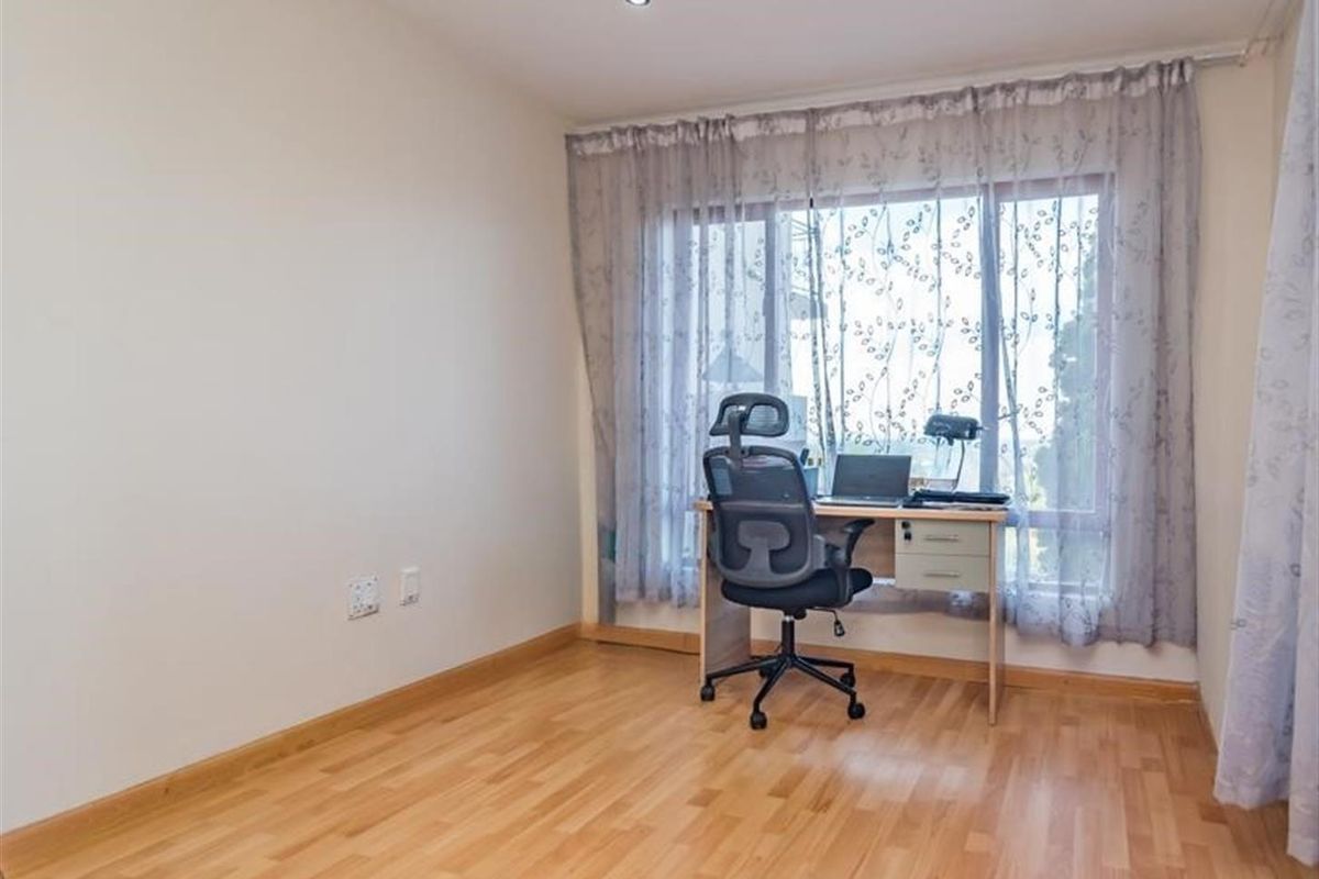 A bright bedroom or home office featuring light wood laminate flooring, recessed ceiling lighting, and a large window with sheer curtains.