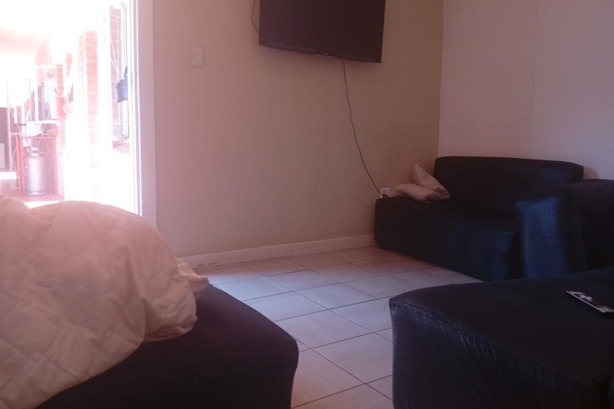 A living room area featuring tiled flooring and a wall-mounted television, with direct access to an outdoor patio space.