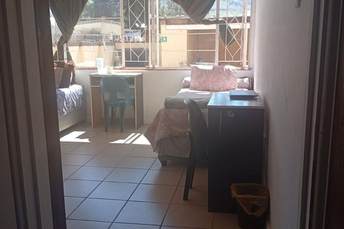 A bedroom featuring tiled flooring and large windows with security bars, offering natural light and a view of the exterior area.