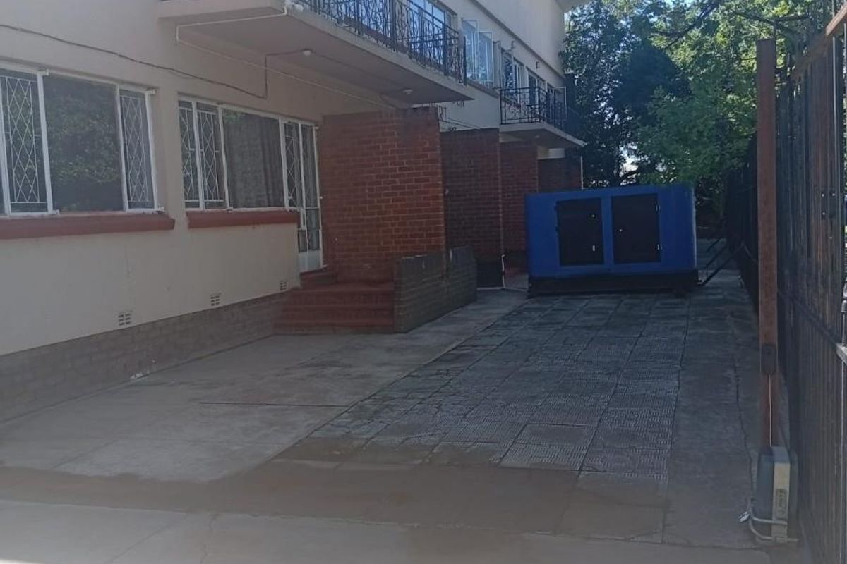 Rear exterior view of the property featuring a paved driveway, brick structural pillars, and upper-level balconies with wrought iron railings.
