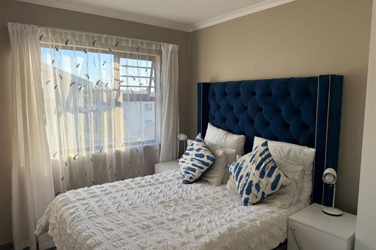 A well-lit bedroom featuring neutral wall tones, a large window with sheer curtains, and tiled flooring.