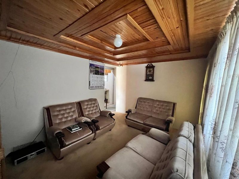 A living room featuring a distinctive timber-clad coffered ceiling and carpeted flooring, showing signs of wear including visible wall cracks.