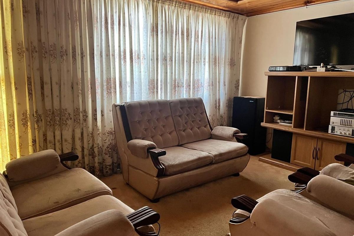 A living room featuring a traditional timber tongue and groove ceiling and carpeted flooring, offering a dated but functional space.