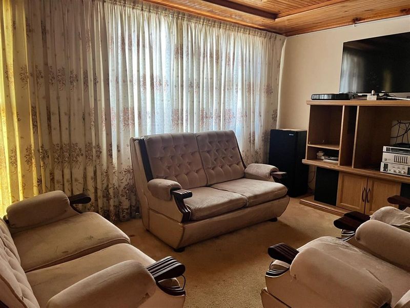 A living room featuring a traditional timber tongue and groove ceiling and carpeted flooring, offering a dated but functional space.