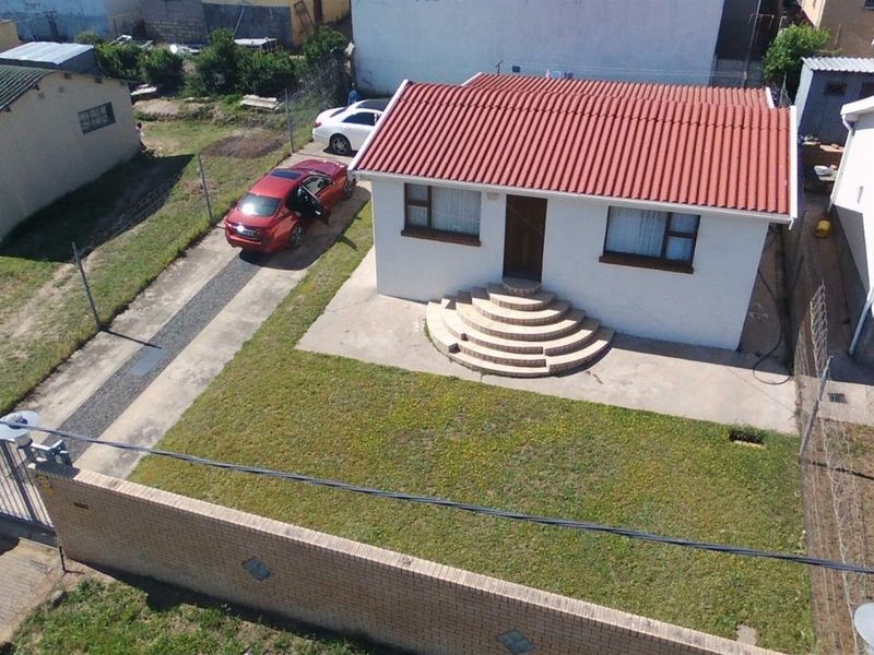 Aerial view of a detached house featuring a corrugated metal roof, concrete driveway, and a front entrance with semi-circular concrete steps.