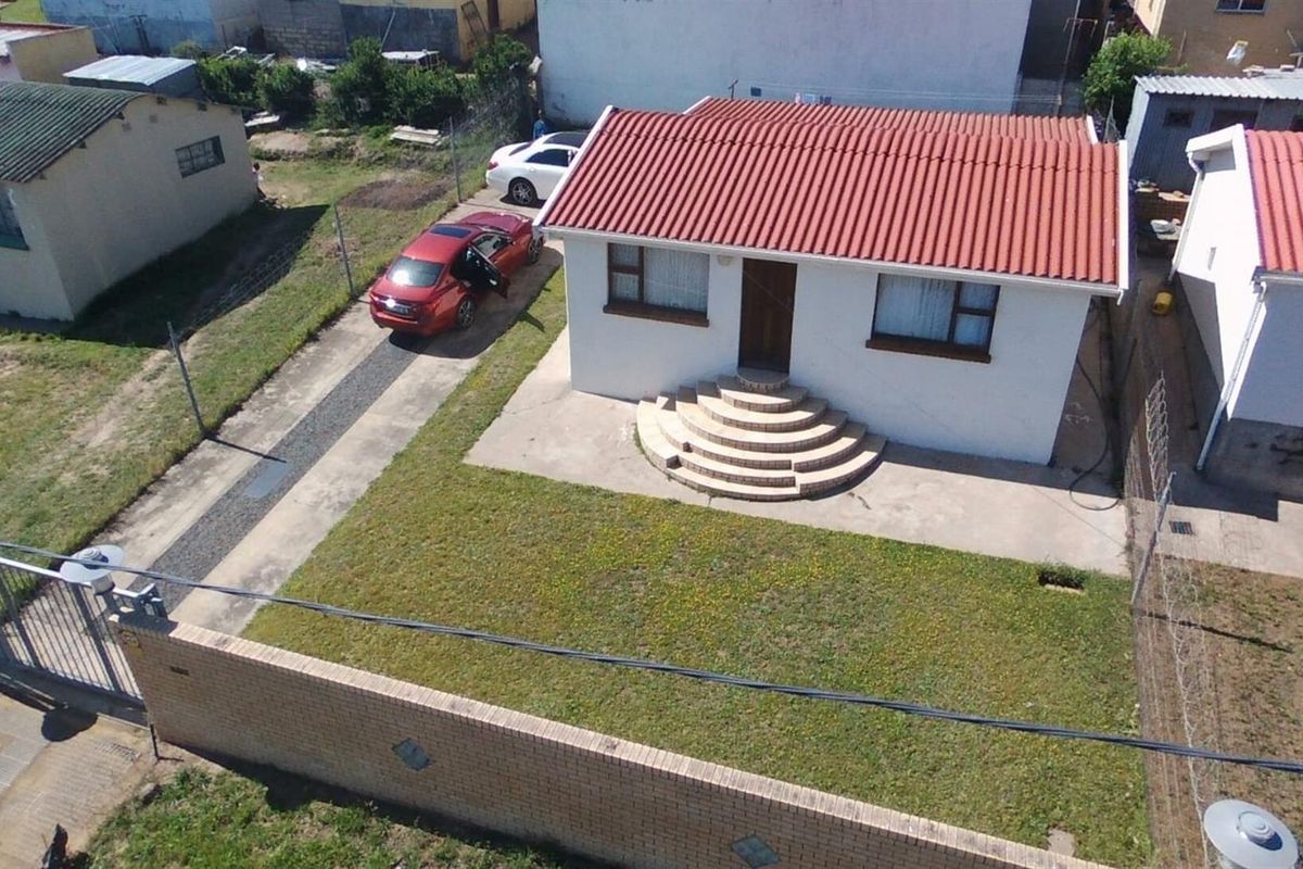 Aerial view of a detached house featuring a corrugated metal roof, concrete driveway, and a front entrance with semi-circular concrete steps.