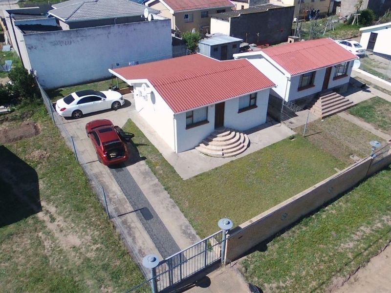 Aerial view of a residential property featuring a corrugated metal roof, concrete driveway, and perimeter wall with gated access.