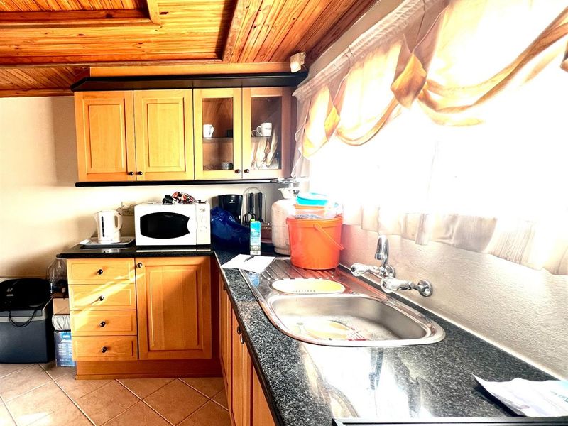 A functional kitchen featuring wooden cabinetry, granite countertops, a stainless steel sink, and a distinctive timber ceiling.