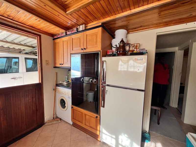 A compact kitchen area featuring wooden cabinetry, a built-in oven, tiled flooring, and a distinctive wooden tongue and groove ceiling.