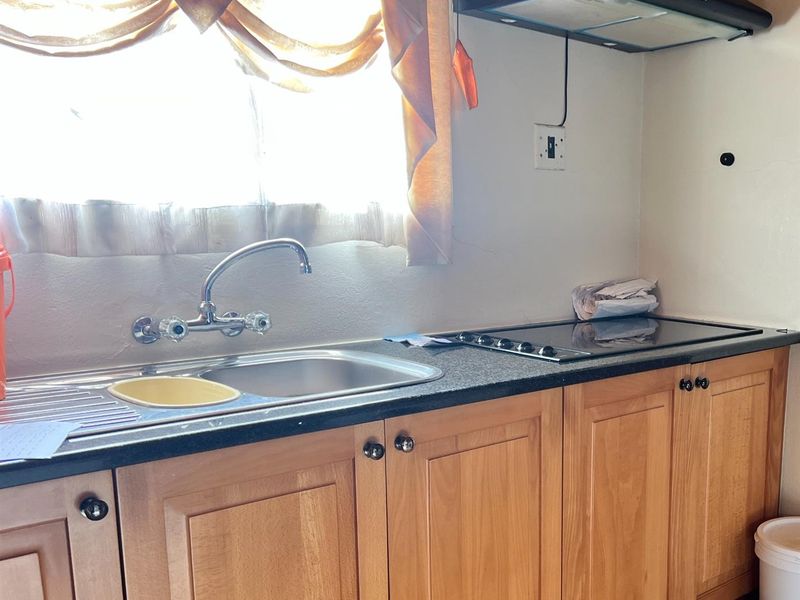 A functional kitchen area featuring wooden cabinetry, a stainless steel sink, and a built-in electric hob with an overhead extractor fan.