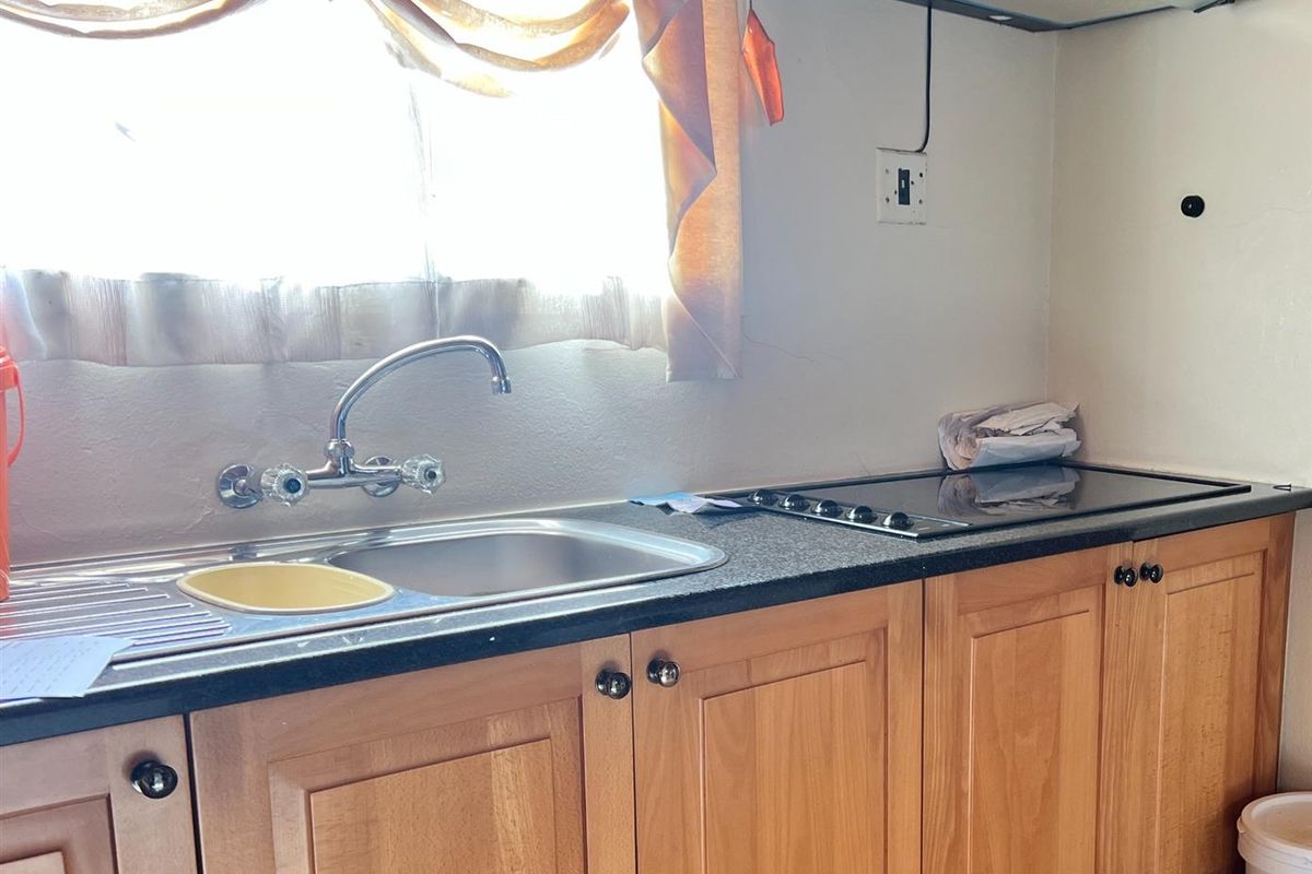 A functional kitchen area featuring wooden cabinetry, a stainless steel sink, and a built-in electric hob with an overhead extractor fan.