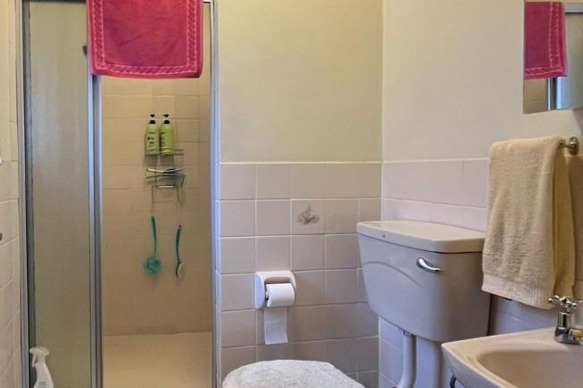 A functional bathroom featuring a shower enclosure, pedestal basin, and toilet with neutral wall and floor tiling.
