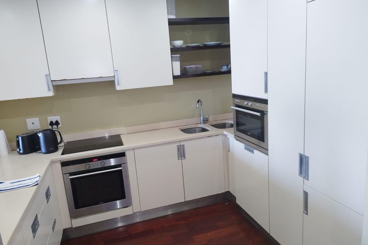 Compact kitchen featuring white cabinetry, integrated oven, electric hob, stainless steel sink, and dark wood-look flooring.