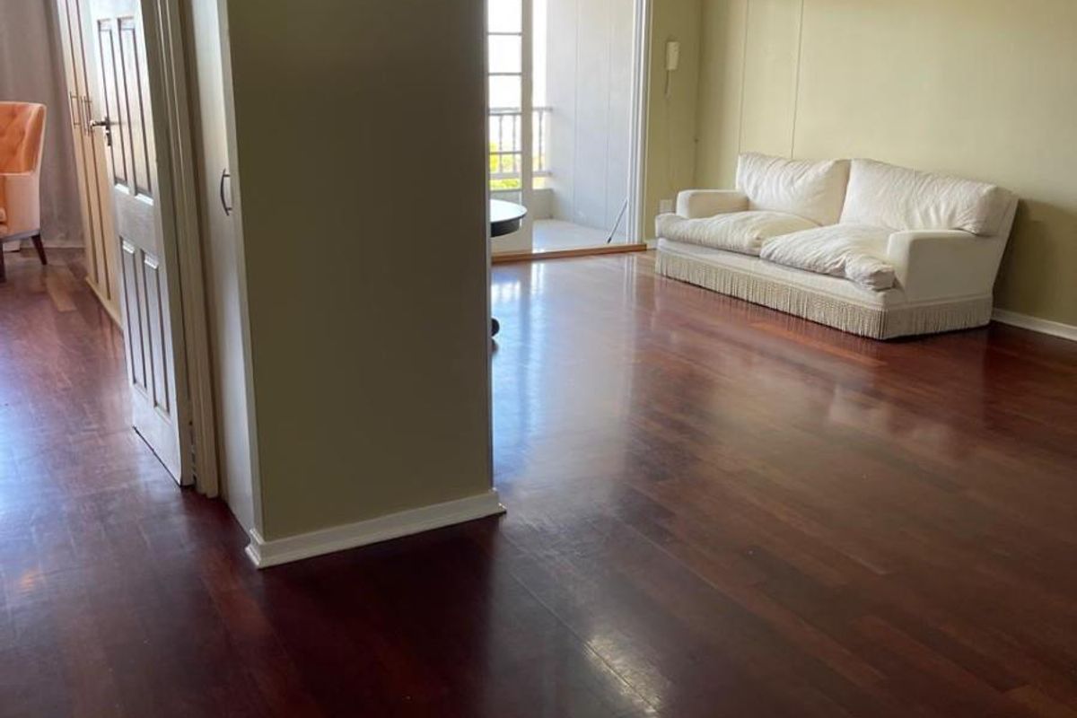 Spacious living area featuring polished hardwood flooring, neutral wall tones, and direct access to a private balcony through glass panel doors.