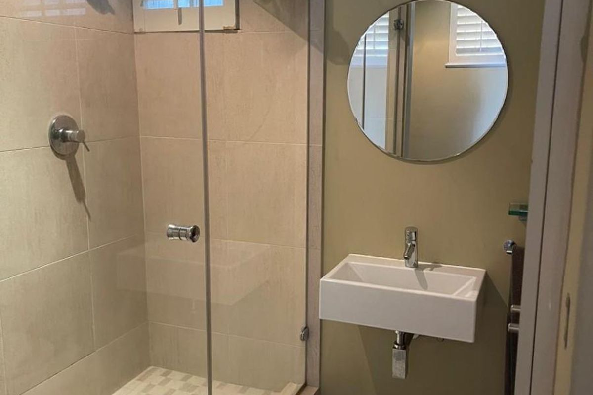 Modern bathroom featuring a glass-enclosed walk-in shower with tiled flooring and a wall-mounted floating basin with a circular mirror.
