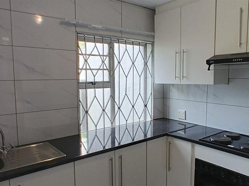 Modern kitchen featuring white cabinetry, dark granite countertops, stainless steel sink, built-in electric hob, oven, and extractor fan with tiled splashback.