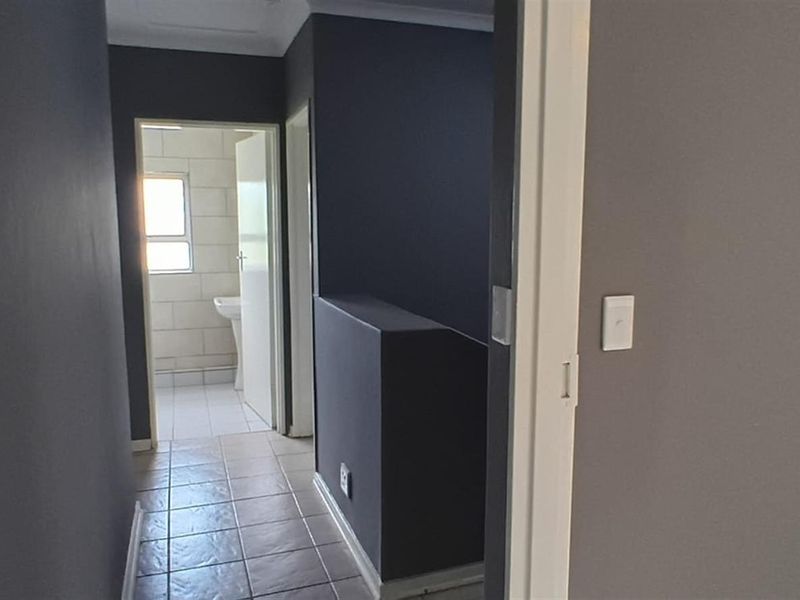 A neutral-toned hallway featuring tiled flooring, leading towards an adjacent bathroom area with natural light.