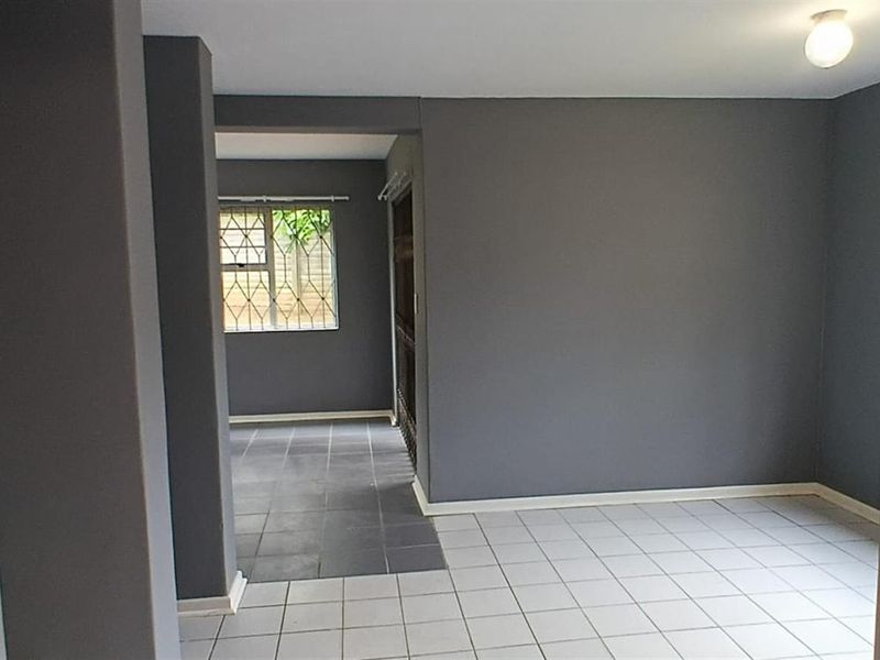 An empty, neutrally painted living area featuring tiled flooring, security bars on the windows, and clean, modern wall finishes.