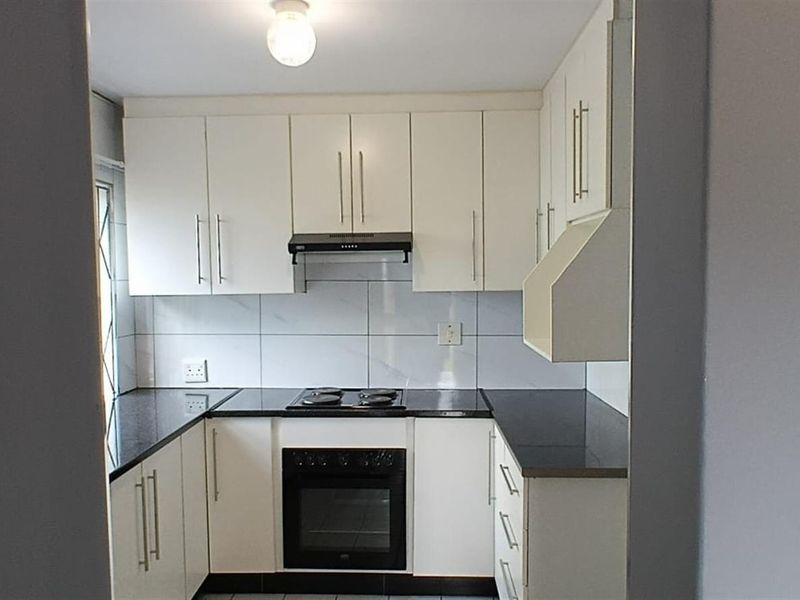 A clean, functional kitchen featuring white cabinetry, black granite countertops, a built-in oven, and an electric hob with a tiled backsplash.