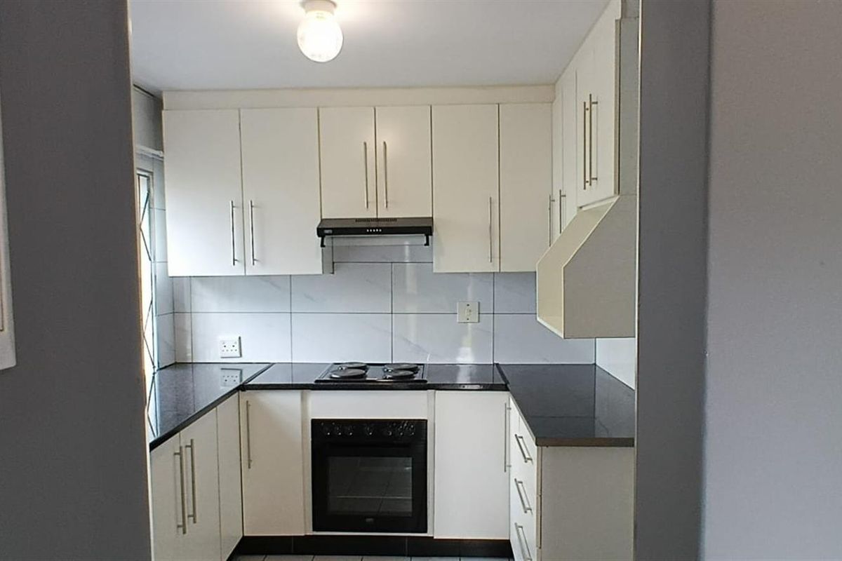 A clean, functional kitchen featuring white cabinetry, black granite countertops, a built-in oven, and an electric hob with a tiled backsplash.